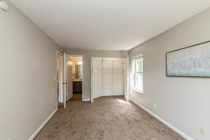 Bright and spacious bedroom with chic carpet flooring, open closet space, and ample natural light.