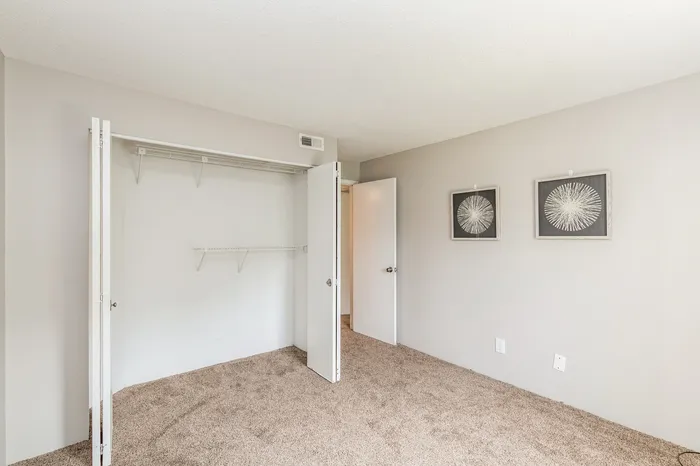 Bright and airy bedroom with plush carpeting, spacious closet, and modern wall art, ideal for serene living.