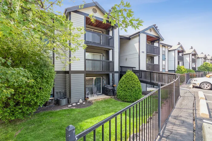 Charming apartment complex with modern balconies, vibrant green landscaping, and welcoming walkways under a clear blue sky.