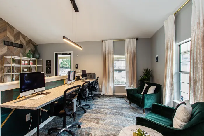 Modern co-working space with stylish green velvet chairs, sleek computer stations, and abundant natural light.