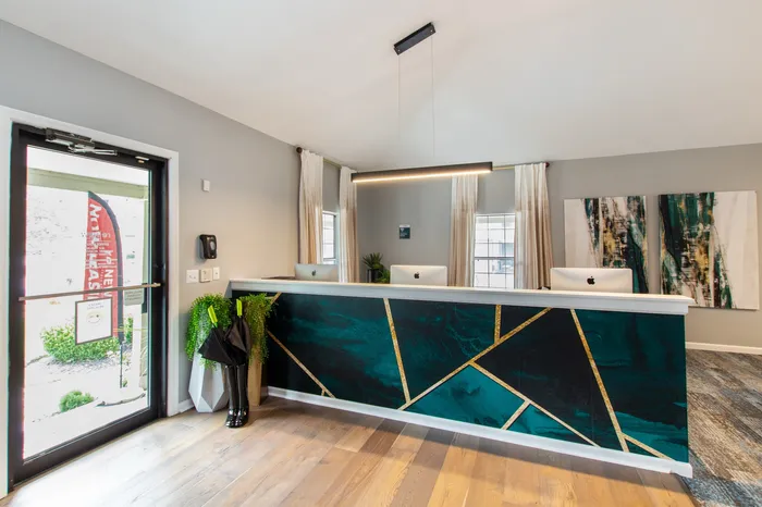 Modern leasing office with elegant teal and gold reception desk, natural light, and stylish decor.