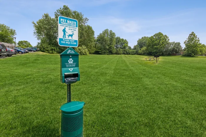Expansive pet-friendly park with lush green grass, equipped with pet waste station and picnic area, perfect for enjoying nature with your furry friends.