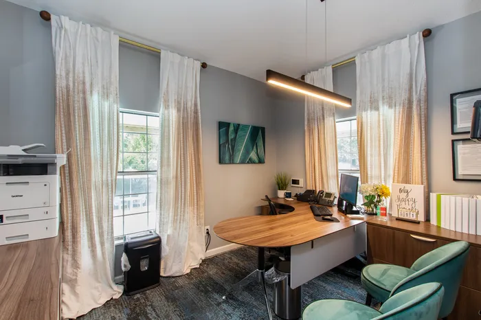 Elegant home office featuring a sleek wooden desk, comfortable teal chairs, and a stylish modern aesthetic with ample natural light.