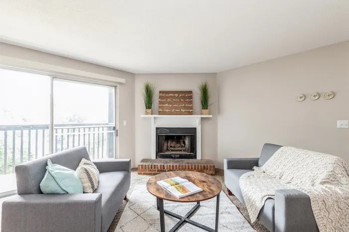 Bright and cozy living room with modern gray sofas, a rustic fireplace, and elegant decor, framed by large windows with a scenic view.