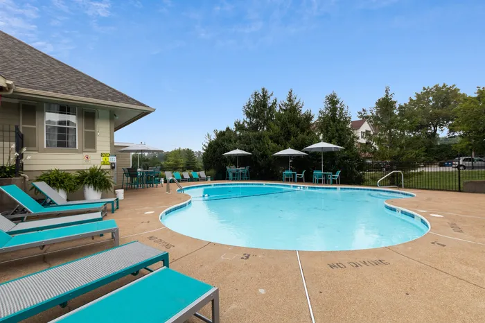 Inviting outdoor pool area with vibrant turquoise loungers, shaded tables, and lush greenery, perfect for relaxation and leisure.