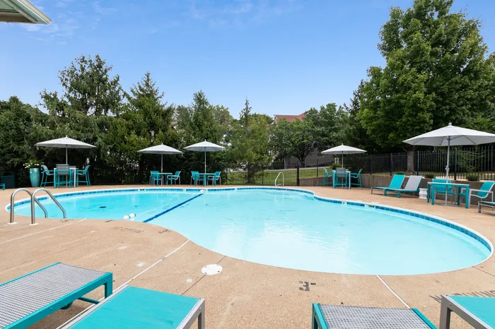 Inviting outdoor pool area with modern lounge chairs and shaded tables, set against lush greenery for a relaxing atmosphere.