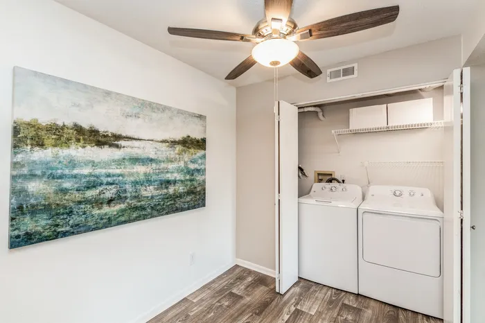 Cozy laundry nook with modern washer and dryer, framed by elegant artwork and contemporary ceiling fan, ideal for efficient living.