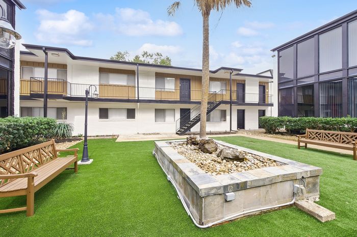 Charming apartment courtyard with lush green lawn, modern architecture, and inviting benches under a sunny sky.