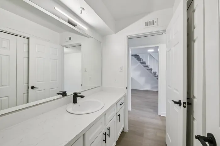 Sleek modern bathroom with elegant countertop, stylish fixtures, and a view of the chic staircase leading to the upper level.