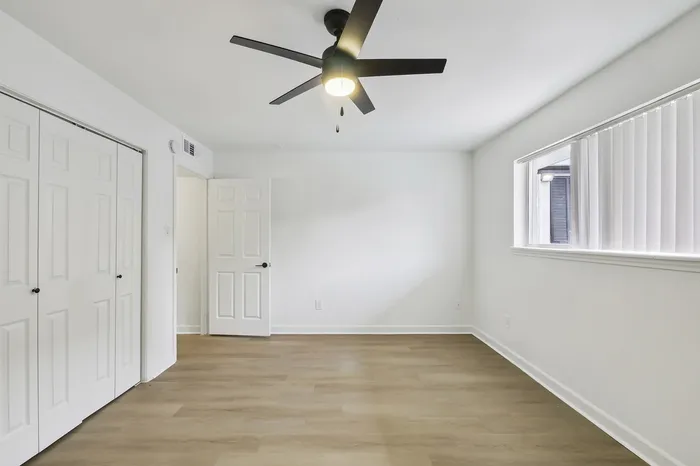 Bright and airy room with modern ceiling fan, sleek wooden floors, and ample closet space.