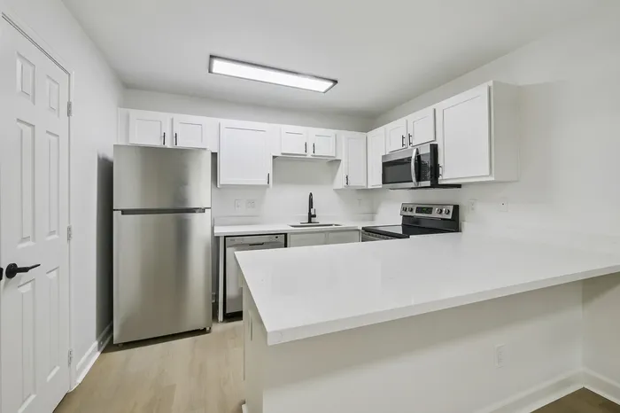 Modern kitchen featuring sleek stainless steel appliances, bright white cabinetry, and a spacious countertop perfect for culinary creativity.