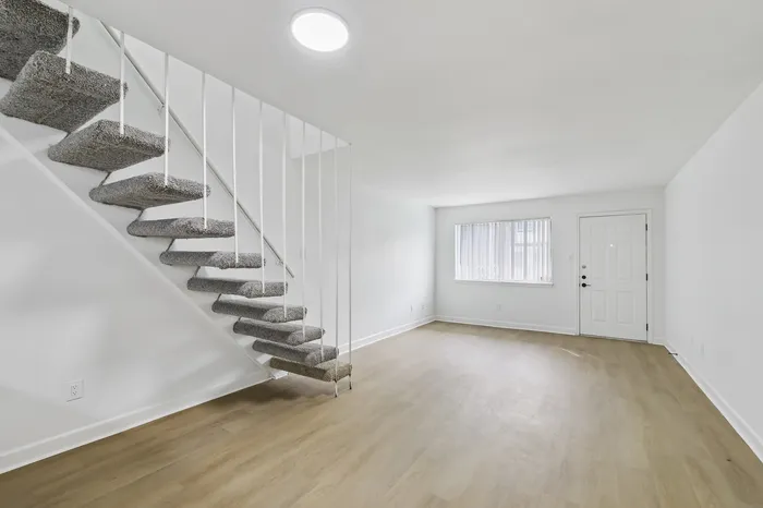 Bright apartment with sleek floating staircase, open living space, and large window offering natural light.