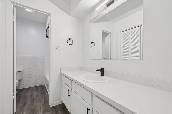 Modern bathroom featuring a sleek white vanity with a black faucet, spacious mirror, and chic wood flooring.