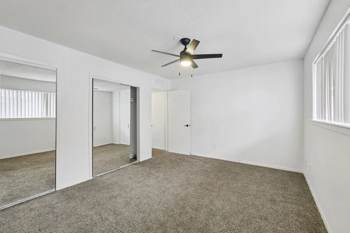 Bright, spacious bedroom with plush carpet, mirrored closet doors, ceiling fan, and ample natural light.