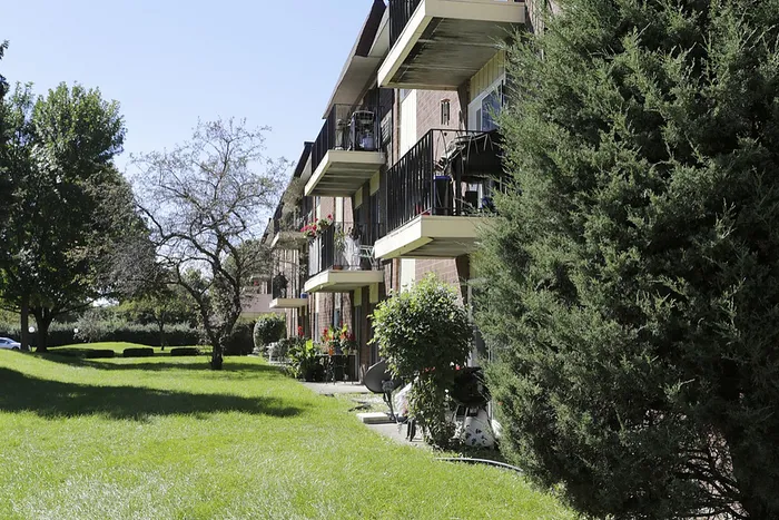 Charming apartment complex with sunlit balconies and lush green lawns, surrounded by mature trees for a tranquil living experience.