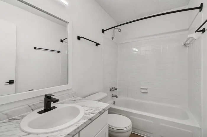 Elegant bathroom featuring a sleek marble countertop, modern black fixtures, and a pristine white bathtub showcasing contemporary design.