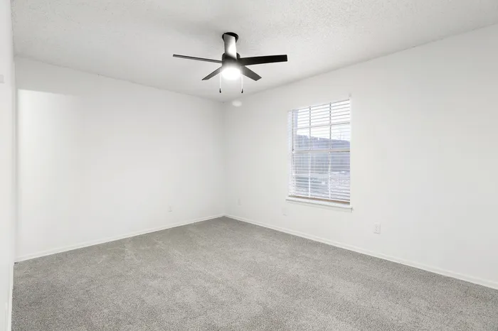 Bright and airy bedroom with plush carpeting, modern ceiling fan, and sunlit window offering tranquil views.
