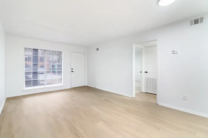 Bright and spacious living area with sleek hardwood floors, large window, and modern white walls.