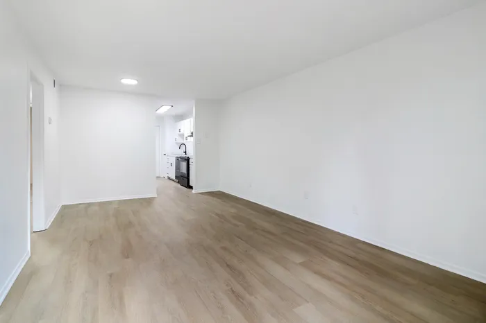 Bright and inviting open-concept living room with elegant wood flooring and a sleek kitchen in the background.