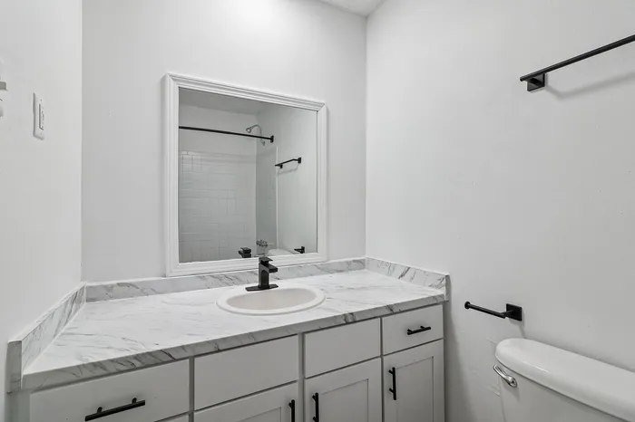 Sleek and modern bathroom with elegant marble countertop, stylish black fixtures, and a large mirror for a luxurious touch.