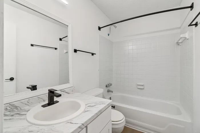 Elegant bathroom with a modern marble vanity, sleek black fixtures, and a pristine white tub and tiles.