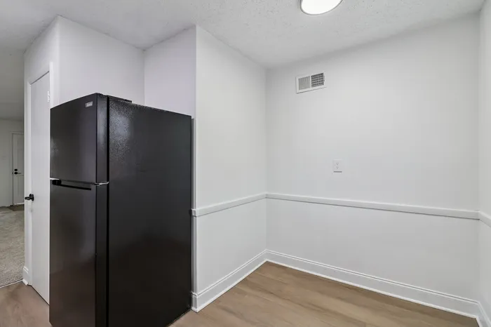 Sleek and modern kitchen corner with a black refrigerator, white walls, and elegant flooring, perfect for urban living.