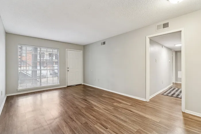 Bright living room with sleek hardwood floors and large window, offering a welcoming entryway view.