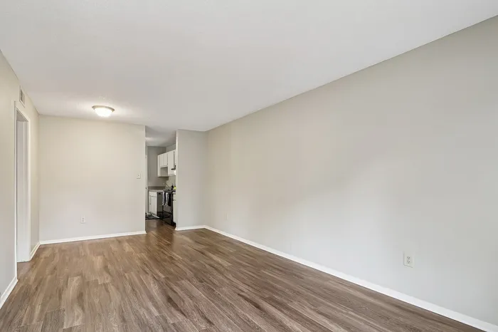 Bright and inviting living area featuring modern wood flooring and access to a cozy kitchen with white cabinetry.
