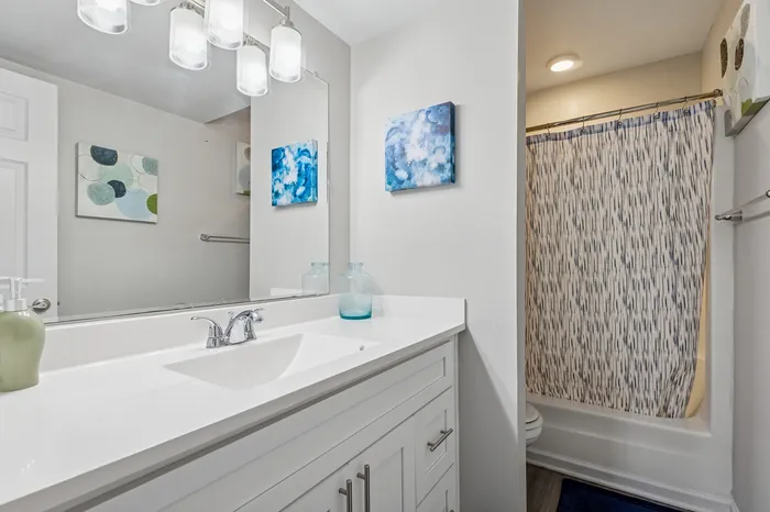Modern bathroom showcasing a sleek white vanity with contemporary fixtures, elegant lighting, and artistic wall decor, complemented by a stylish shower curtain.