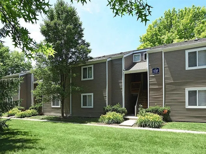 Charming apartment building surrounded by lush greenery and vibrant shrubs, featuring modern siding and large windows.