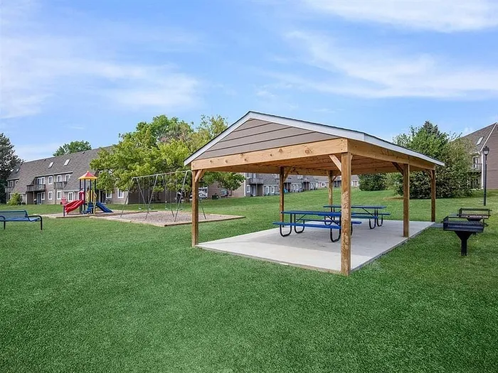 Charming apartment complex with a vibrant playground, shaded picnic area, and lush green lawn.