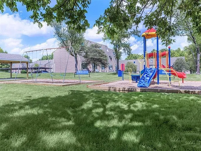 Charming community playground with vibrant play structures surrounded by lush green lawns and nearby residential buildings.