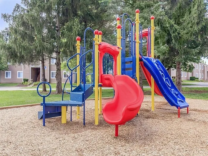 Vibrant playground featuring colorful slides and climbing structure set in a serene apartment community, surrounded by lush greenery.