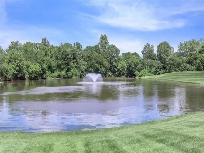 Serene lake view with a picturesque fountain amidst lush greenery and clear blue skies.