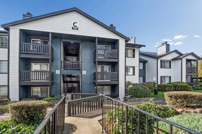 Modern apartment building featuring multiple balconies, lush landscaping, and a welcoming entrance under a clear blue sky.