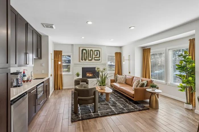 Elegant open-plan living space with a cozy fireplace, stylish brown leather sofa, modern kitchen, and warm natural lighting.