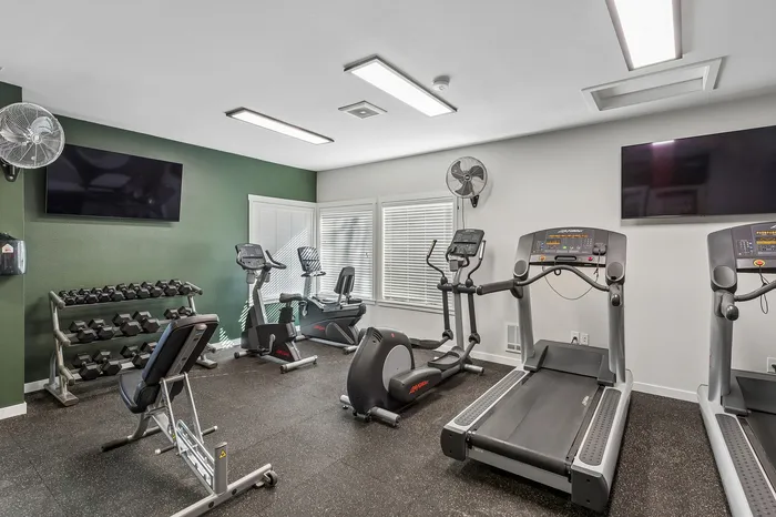 Modern fitness room equipped with treadmills, exercise bikes, weights, and wall-mounted TVs, perfect for a convenient workout at home.