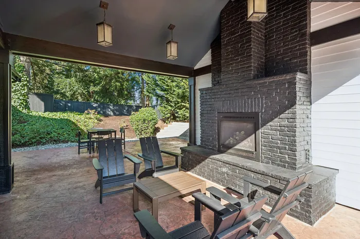 Inviting outdoor patio with stylish seating and a chic brick fireplace, surrounded by lush greenery for a tranquil retreat.