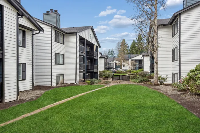 Charming apartment complex with lush green lawns and well-maintained landscaping surrounded by modern white buildings.