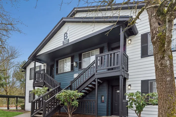 Charming two-story apartment building with a classic navy and white facade, surrounded by lush greenery and vibrant trees.