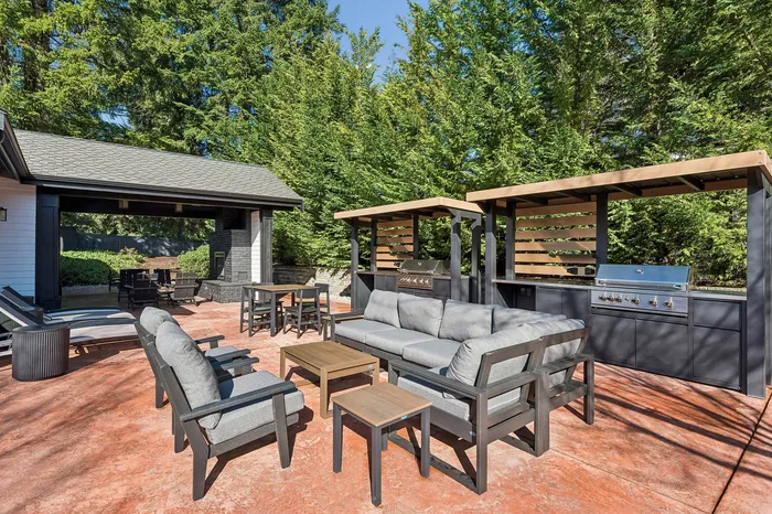 Inviting outdoor living space featuring modern patio furniture, a cozy lounge area, and a sleek built-in grill surrounded by lush greenery.