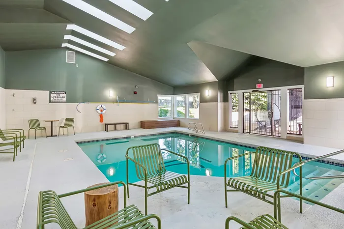 Elegant indoor pool area with skylights, stylish seating, and natural light from large windows.