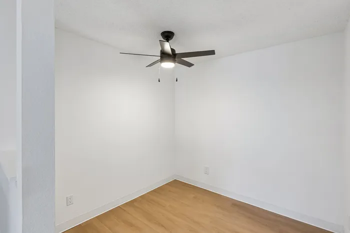 Bright and airy room with modern ceiling fan, pristine white walls, and elegant wood flooring.