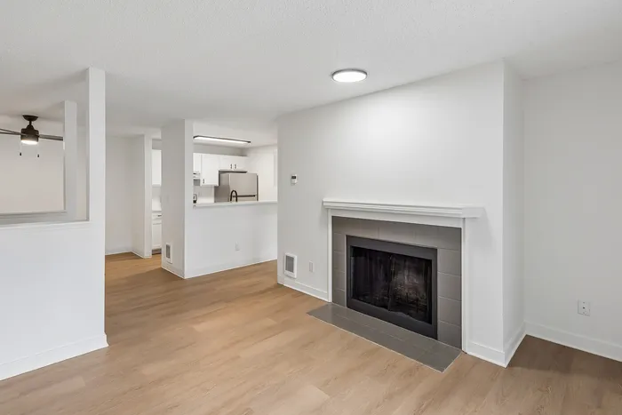 Inviting living space with elegant fireplace and modern open kitchen design, featuring sleek white cabinets and stainless-steel appliances.