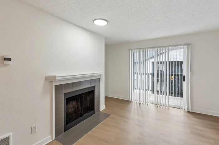 Bright living room featuring a modern fireplace and large sliding glass doors with vertical blinds, offering ample natural light and a cozy atmosphere.