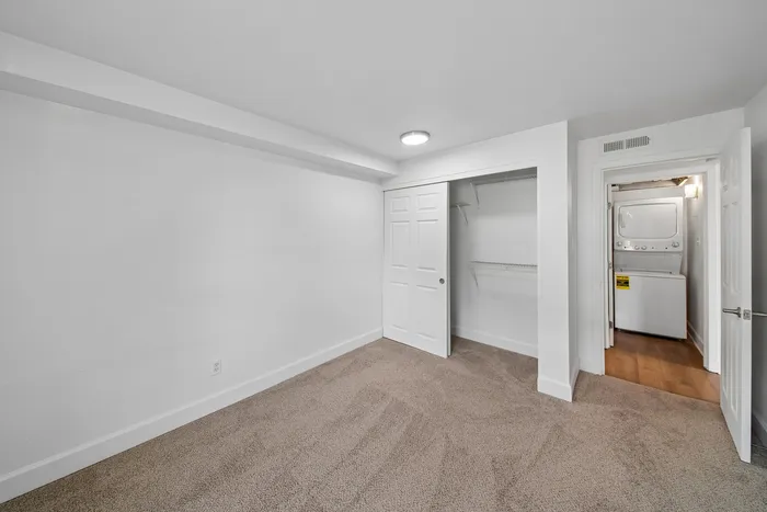 Bright bedroom with plush carpeting, spacious closet, and in-unit laundry area for convenient living.