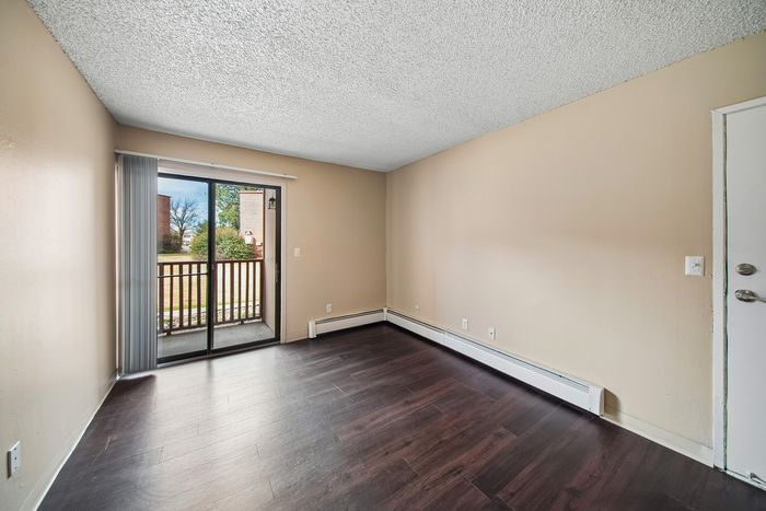 Bright and airy room with elegant dark hardwood floors, sleek sliding glass doors leading to a charming balcony with lush outdoor views.