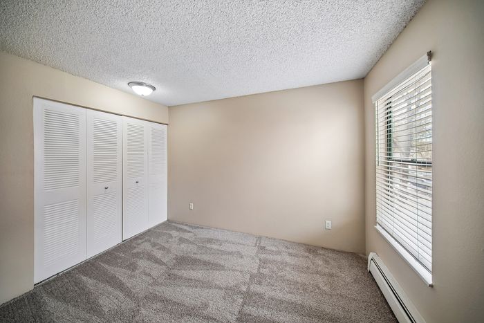 Bright, spacious bedroom with fresh carpeting, large window with blinds, and ample closet space.