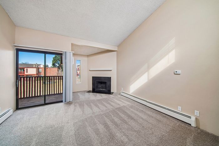 Spacious living room featuring large sliding glass doors leading to a balcony, plush carpeting, and a cozy fireplace with natural light enhancing the charming ambiance.
