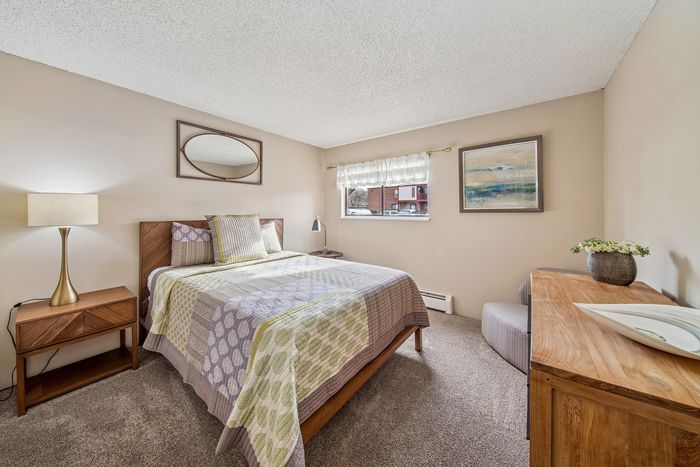 Inviting bedroom featuring a cozy bed with patterned quilt, warm lighting, and modern wooden furniture.